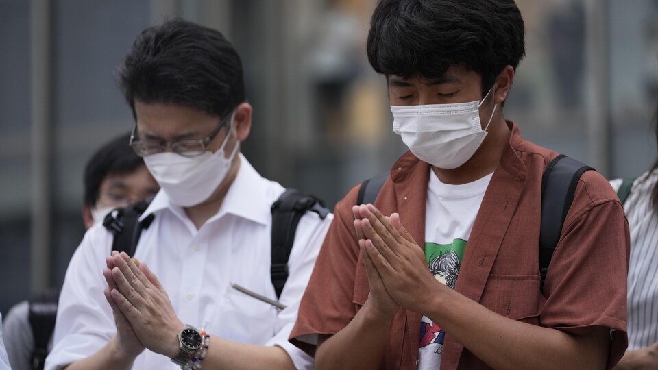 Des Japonais masqués, les mains jointes en prière.