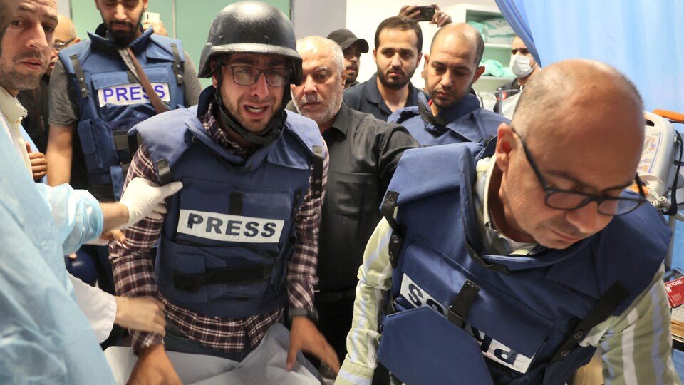 Des hommes portant des vestes sur lesquelles on peut lire le mot « presse » et des membres du personnel médical sont rassemblés autour d'une civière.