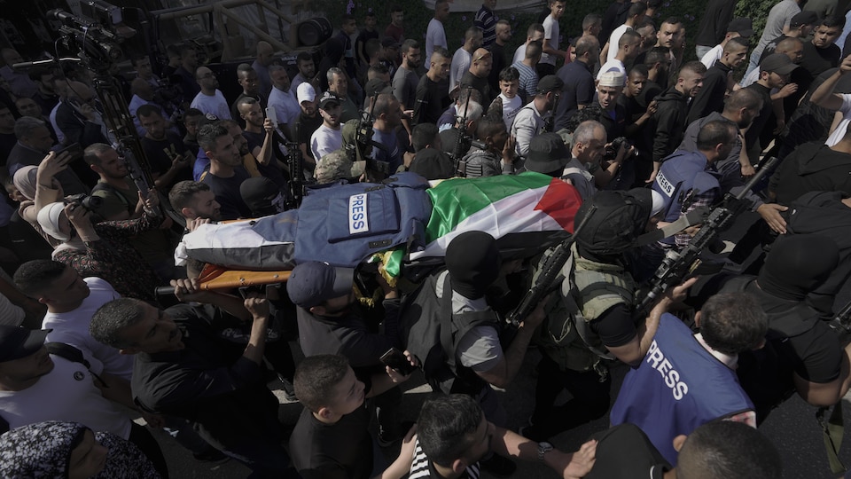 Une foule transporte un brancard sur lequel repose un corps recouvert d'un drapeau palestinien et d'un gilet pare-balles. 