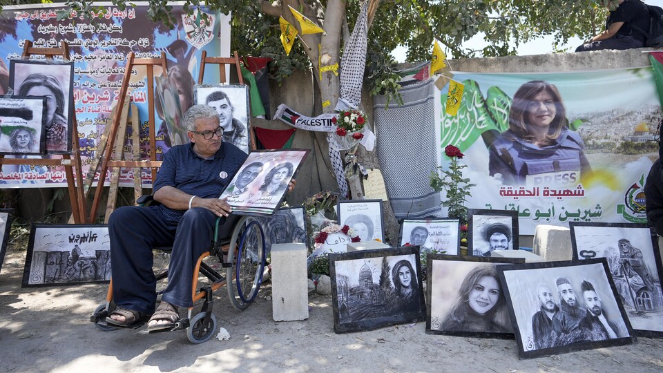 A man in a wheelchair in front of a site where there are drawings or posters showing the murdered journalist.