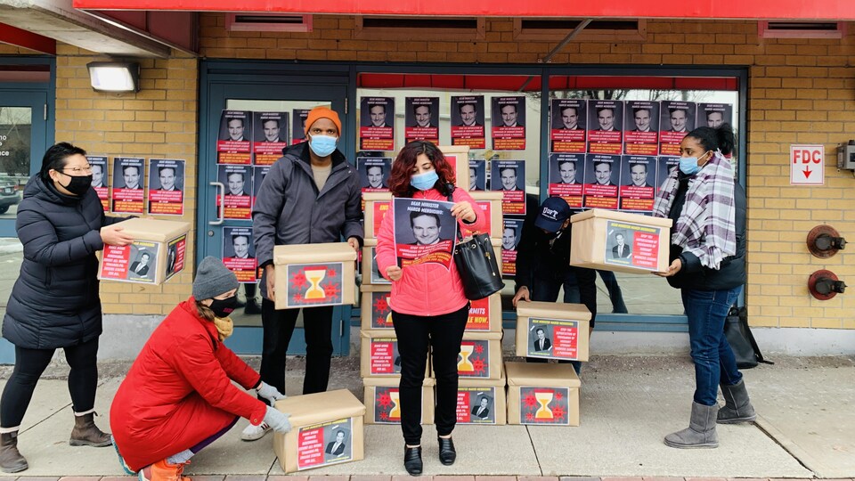 Une femme et un groupe de militants tiennent des boîtes de pétitions devant le bureau du ministre Marco Mendicino, à Toronto.