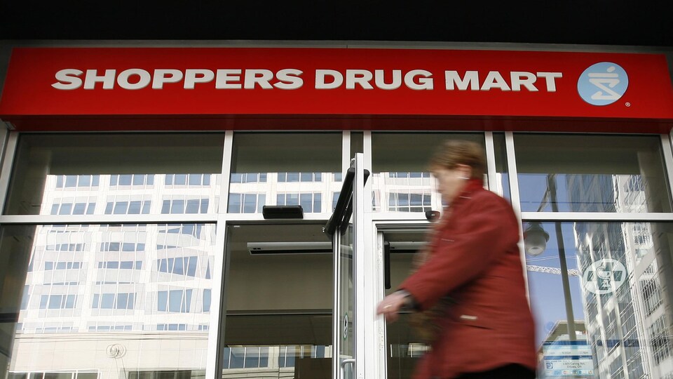Une piétonne passe devant un commerce Shoppers Drug Mart.