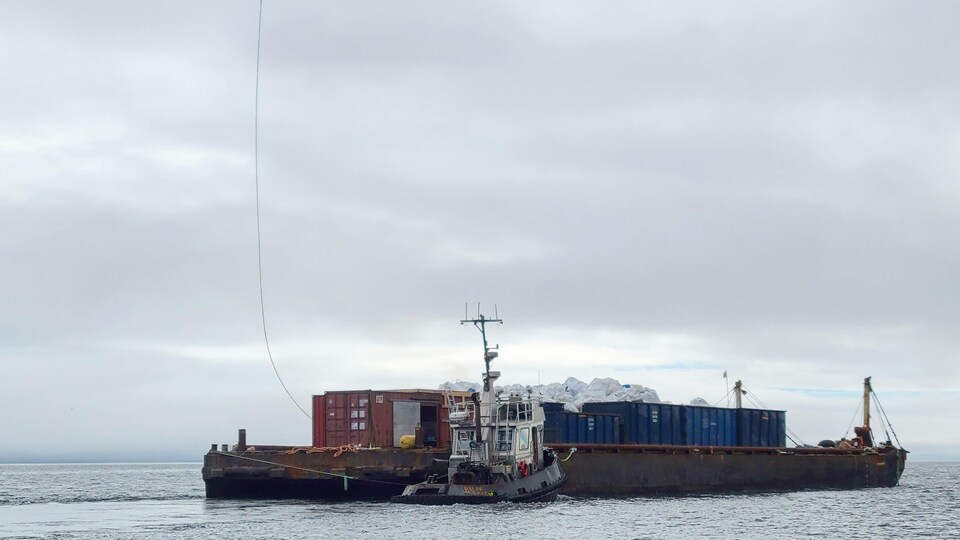 Un hélicoptère survole une barge et un bateau. 