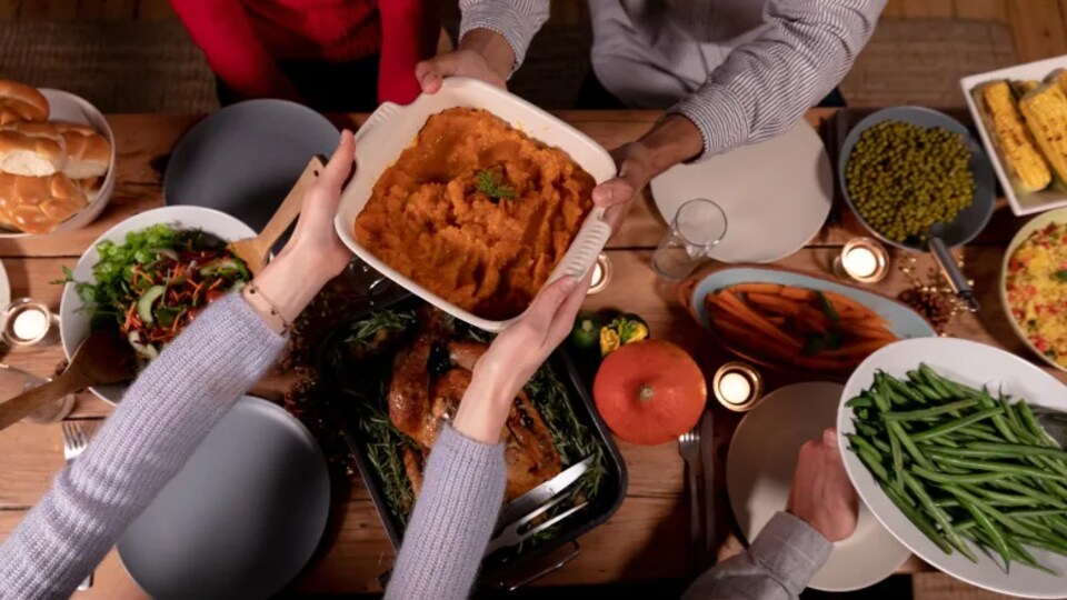 Des gens s'échangent des plats à une table remplie de nourriture.