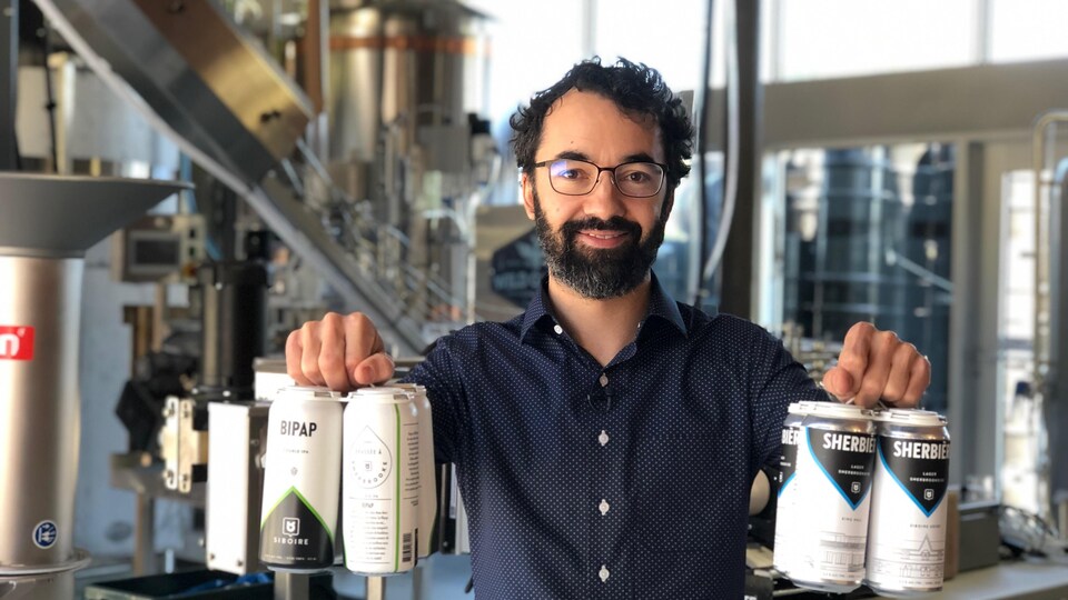 le propriétaire pose devant les silos de bières et présente ses canettes