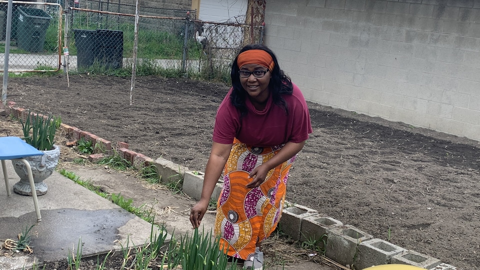 Une femme est dans son jardin. Elle tient une plante.
