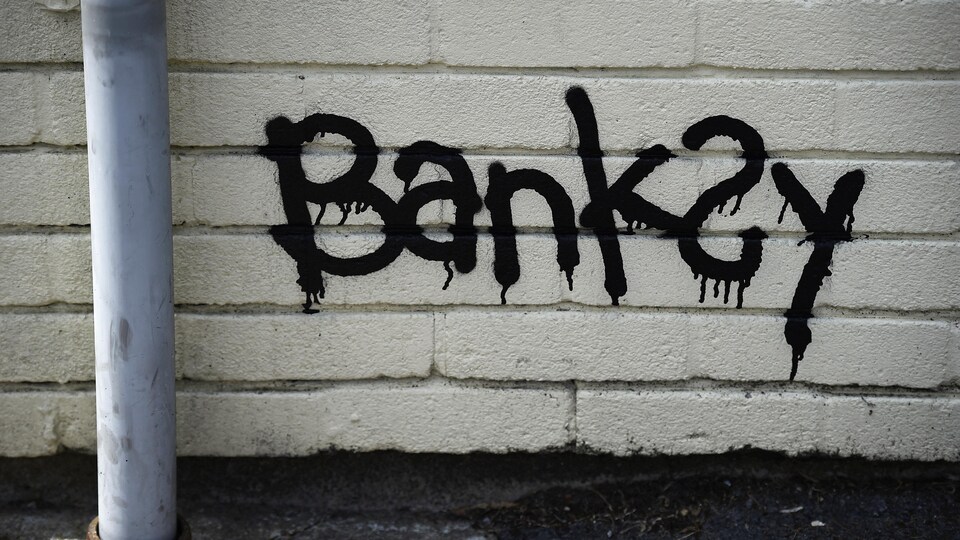 Le nom de Banksy est écrit en noir sur un mur.