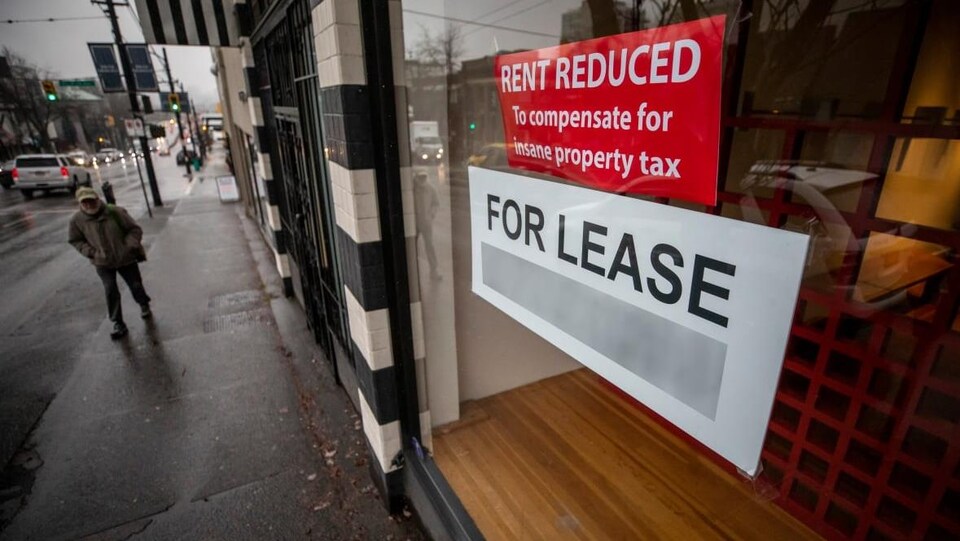 Une affiche dans une vitrine, sur laquelle il est inscrit, en anglais, "loyer réduit pour compenser l'impôt foncier insensé."