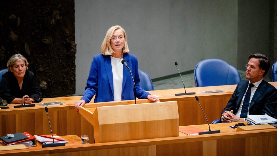 Sigrid Kaag debout derrière un lutrin, avec une autre femme et un homme assis à ses côtés.