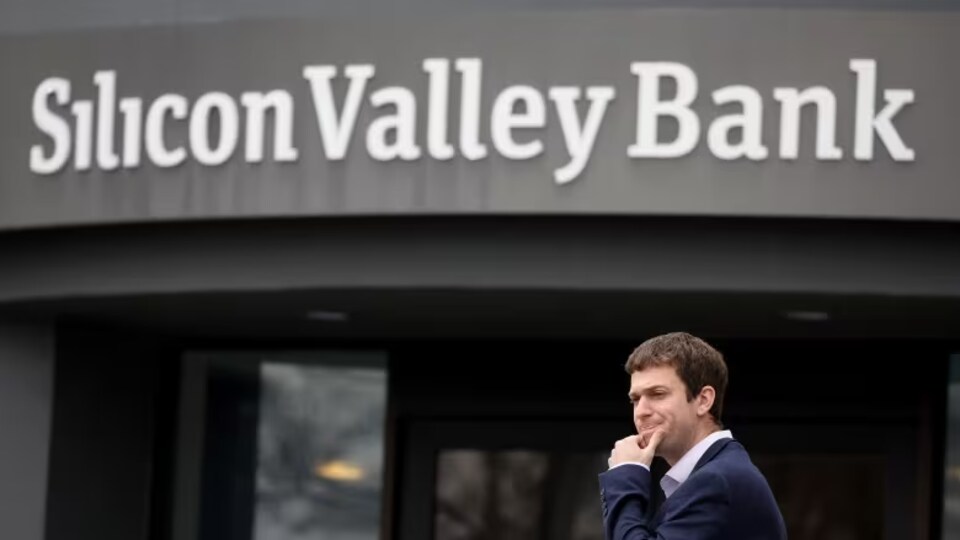 Devant une succursale de la Silicon Valley Bank, un jeune homme en costume sombre a l'air inquiet.
