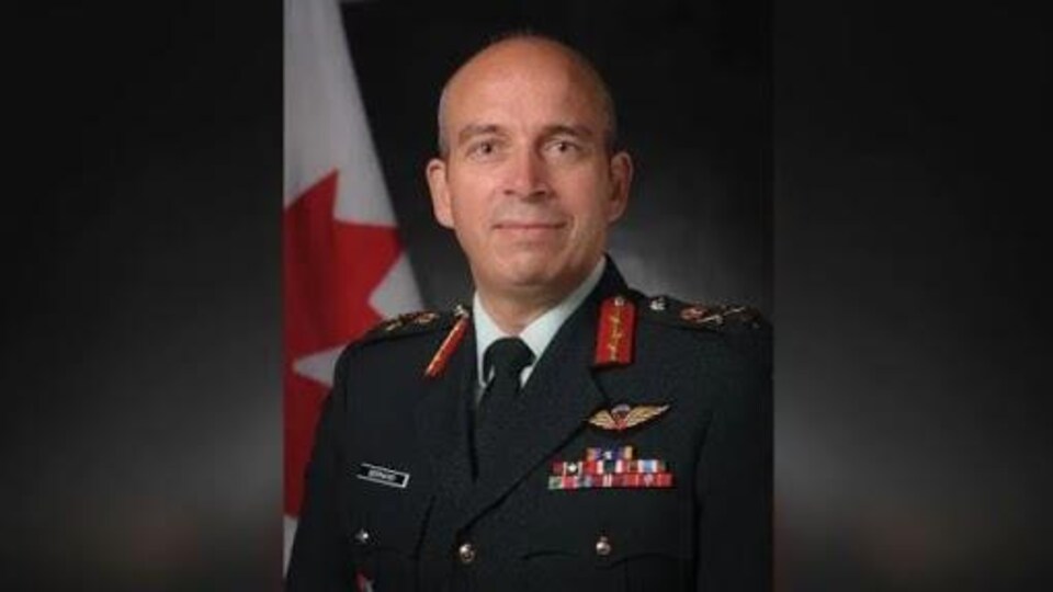 Un militaire en uniforme devant un drapeau du Canada.