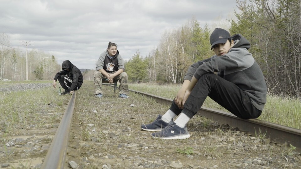 Trois jeunes assis sur un chemin de fer.