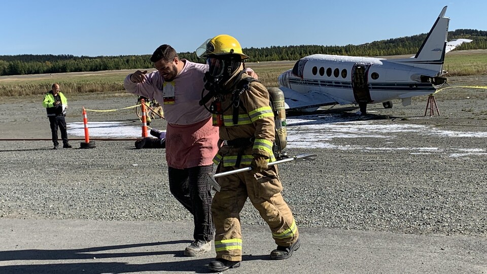 Un pompier escorte un figurant lors de la simulation d’un atterrissage d’urgence avec sortie de piste.