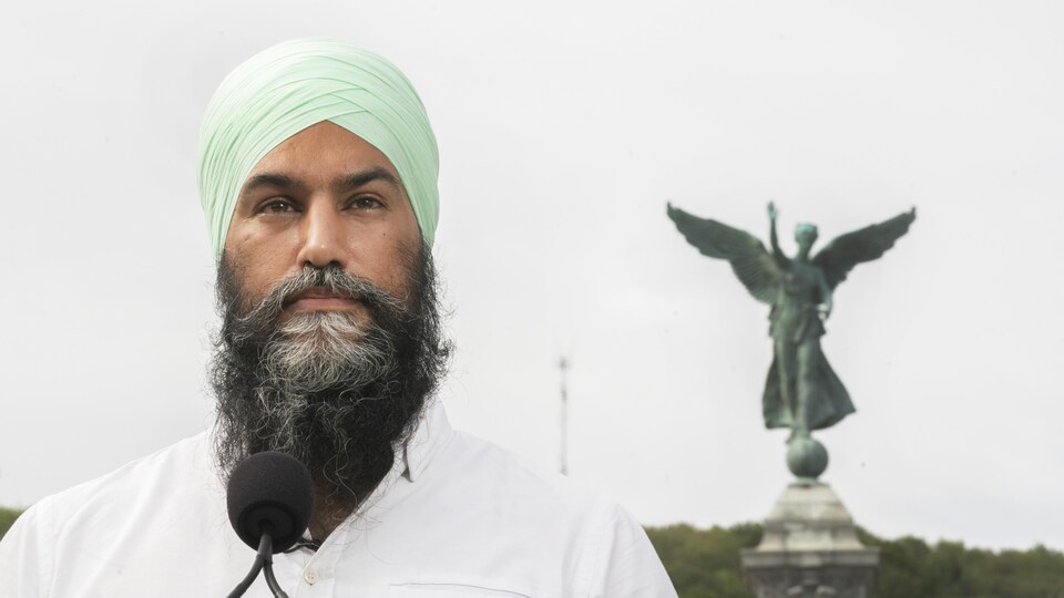 Gros plan de Jagmeet Singh derrière un micro et devant une statue.