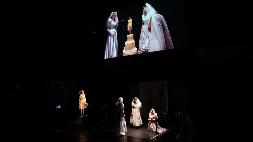 Capture d'écran d'une scène de la pièce avec trois femmes portant des robes de mariées.