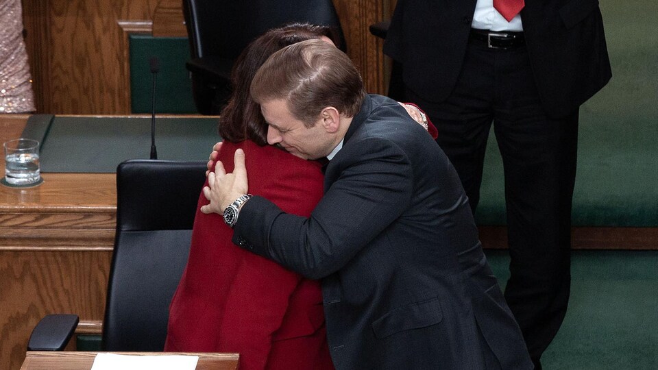 Andrew Furey et Siobhán Coady se donnent l'accolade à la Chambre d'assemblée, pendant que les députés qui les entourent applaudissent. 