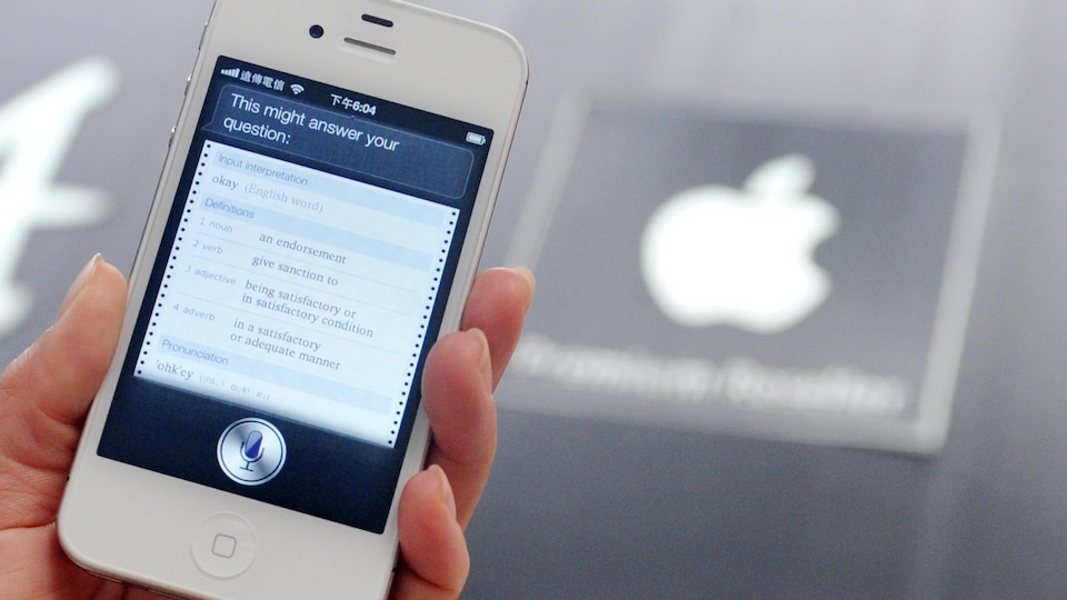 Une main tient un iPhone qui affiche l'interface de l'assistant vocal Siri.