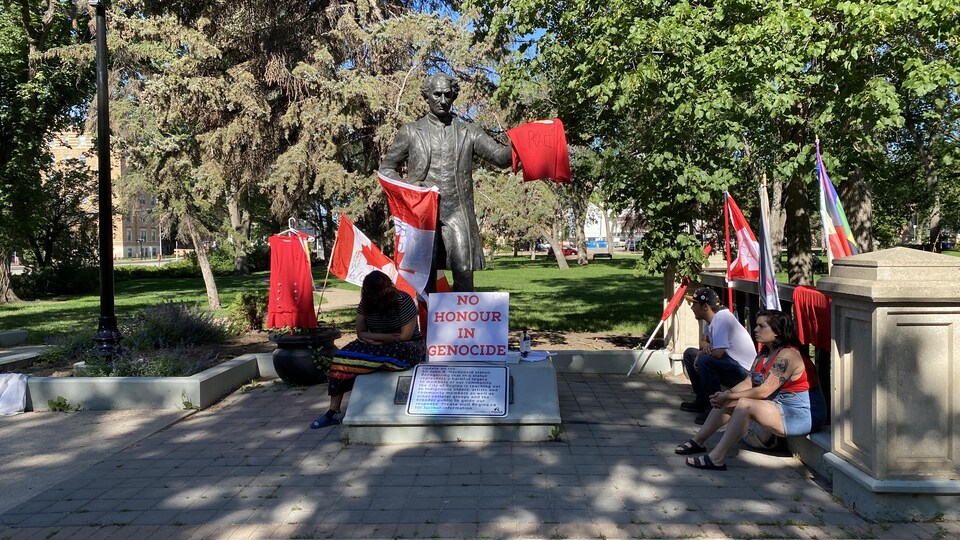 Des manifestants devant la statue de John A. Macdonald au parc Victoria à Regina.