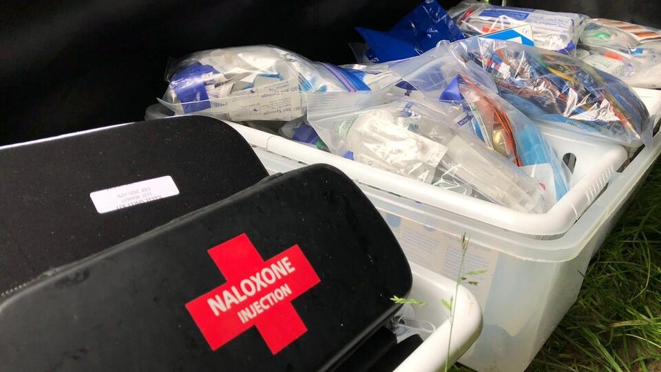 Des bacs en plastique installés à même le sol contiennent des trousses de naloxone et du matériel médical du type auguilles et pansements
