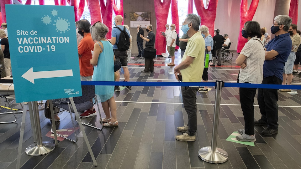 Des gens font la file à l'intérieur d'une clinique de vaccination aménagée au Palais des congrès de Montréal.