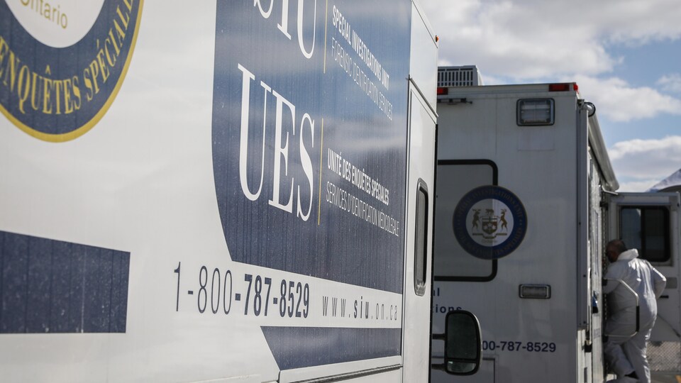 Deux camions de l'unité des enquêtes spéciales de l'Ontario, un homme rentre dans l'un d'entre deux. 
