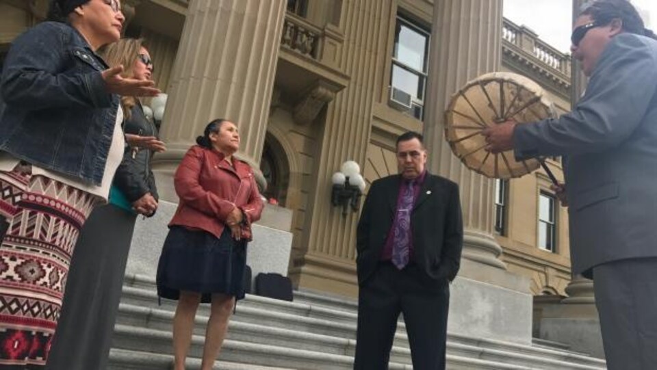 Quatre personnes en cercle dont une qui a un tambour dans les mains devant l'assemblée législative de l'Alberta