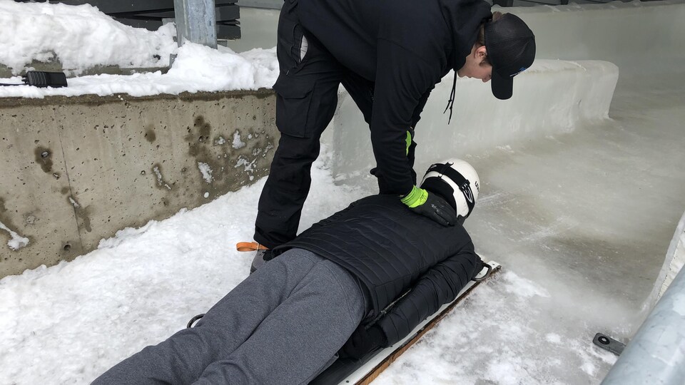 un homme debout pousse un autre homme allongé sur une plache de glisse.