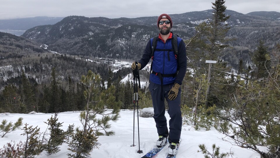 Maxime Bolduc équipé en ski au sommet des nouvelles pistes à Petit-Saguenay, avec vue sur le fjord.