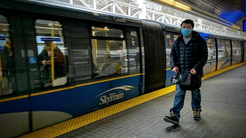 Un homme porte un masque et attend le prochain train.
