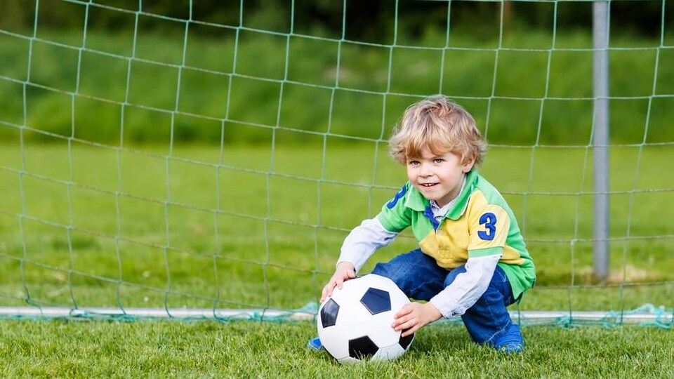 A child holds a soccer ball in front of a net. 