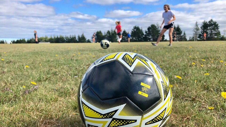 Un ballon de soccer en avant plan avec des jeunes joueuses en arrière plan