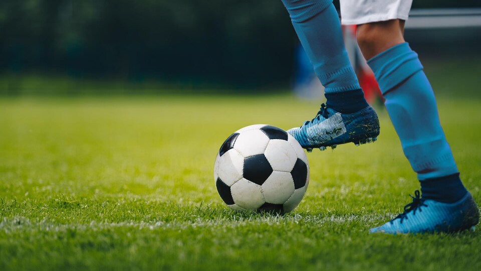 Plan au dessous des genoux d'un joueur de soccer, qui a le pied sur un ballon.