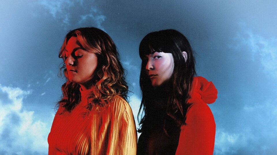 Les deux chanteuses posent côte à côte sur un fond de ciel nuageux.