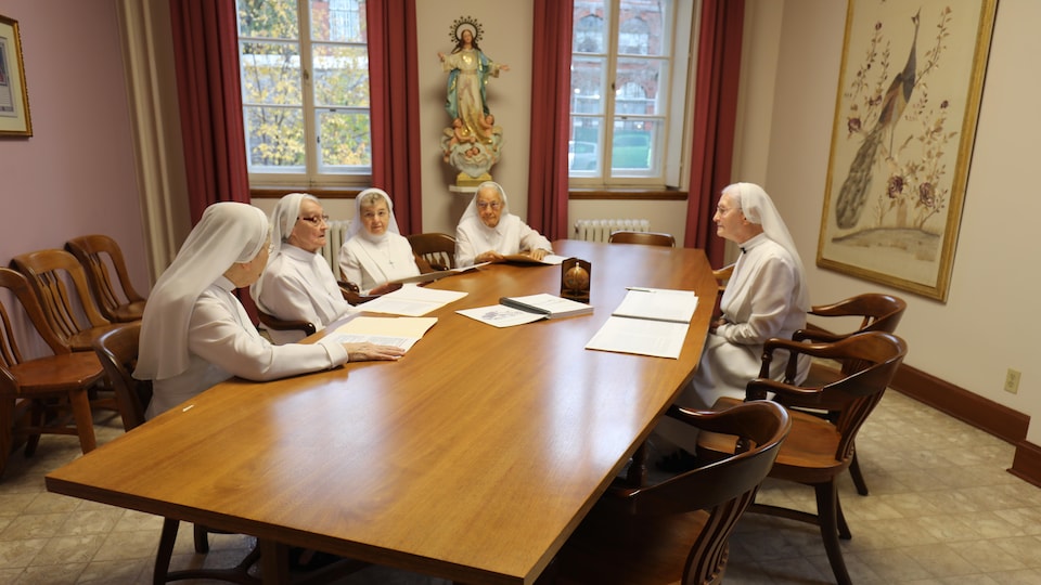 Des soeurs autour d'une table dans une salle avec une statue religieuse