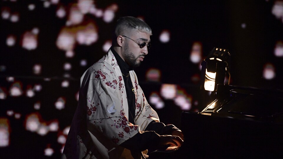 Un homme joue au piano sur scène, dans une ambiance sombre éclairée par quelques lumières. 