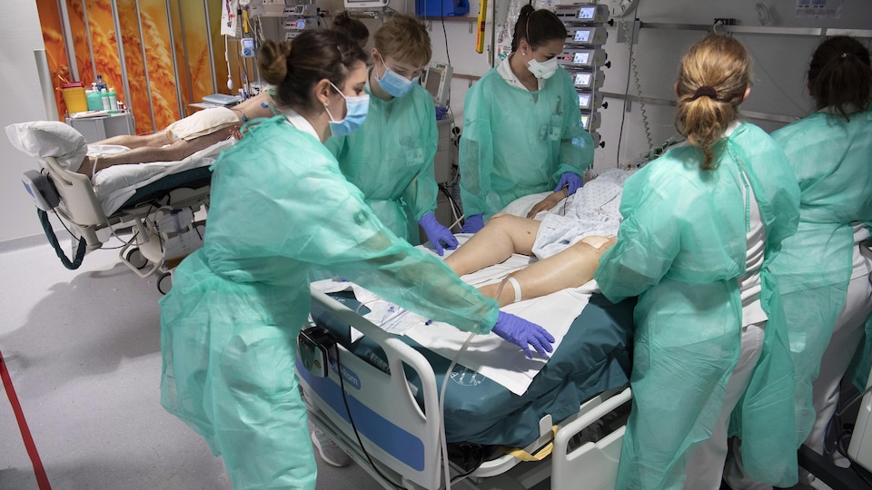 Des infirmières qui portent de l'équipement de protection traitent un patient atteint de la COVID-19.