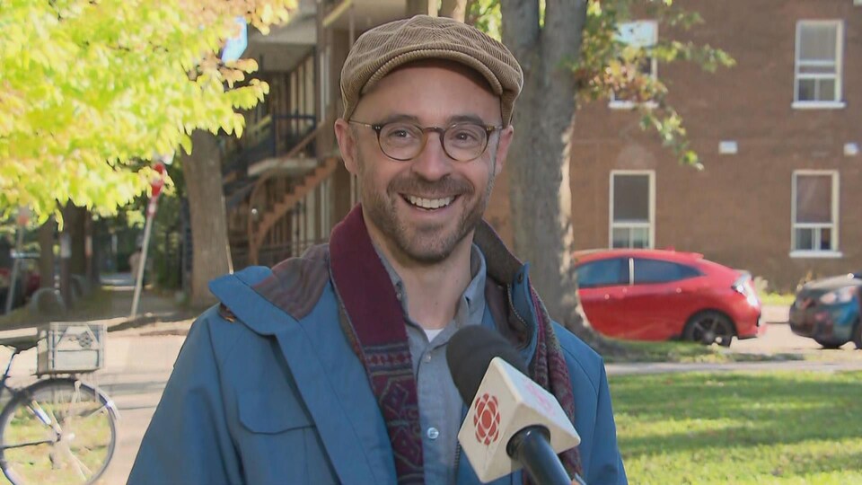 Un homme avec une casquette et qui porte des lunettes en entrevue dehors face à la caméra.