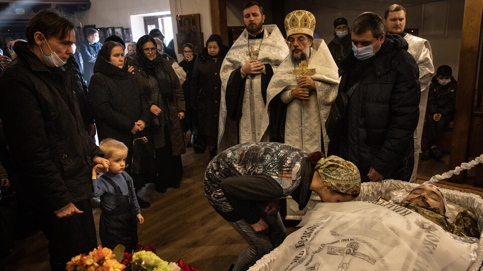 Une femme embrasse le cadavre d'un homme, sous le regard de plusieurs personnes, dont des prêtres orthodoxes.