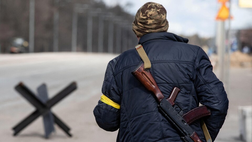 Un homme de dos avec un Kalashnikov en bandoulière.