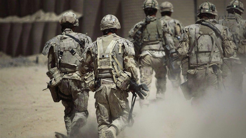 Des soldats en habit de camouflage marchent dans la poussière. Ils sont photographiés de dos.
