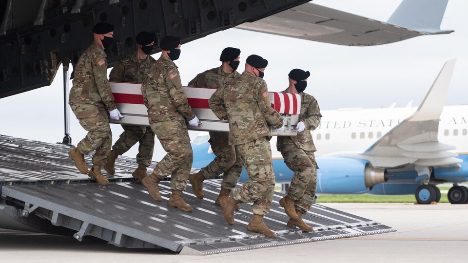 Des militaires tiennent un cercueil et le sortent d'un avion.