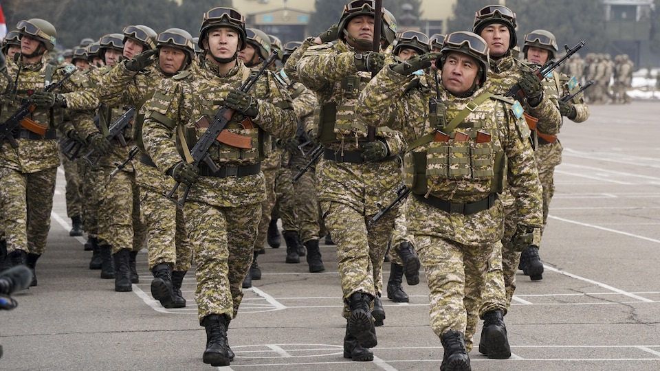 Des soldats en treillis militaires et armés marchent au pas.