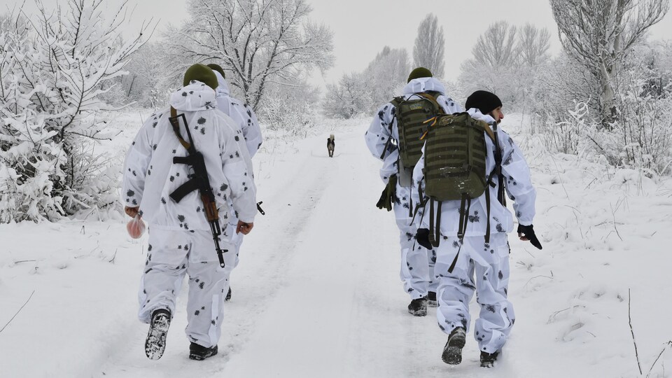 De soldats et un chien marchent dans un chemin ennneigé.