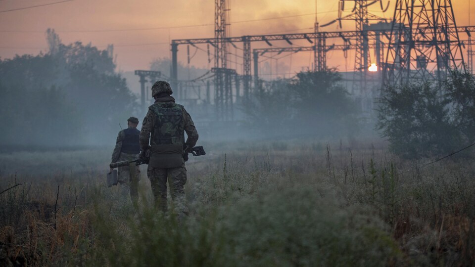 Deux soldats marchent sur un terrain dans une zone industrielle. 