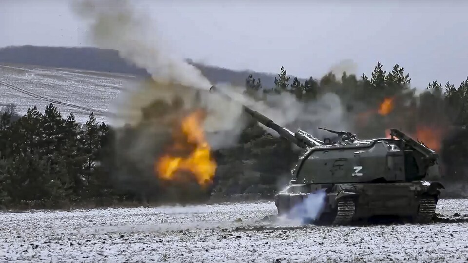 Un char d'assaut marqué d'un « zèd » tire un coup de canon à partir d'un champ en hiver.