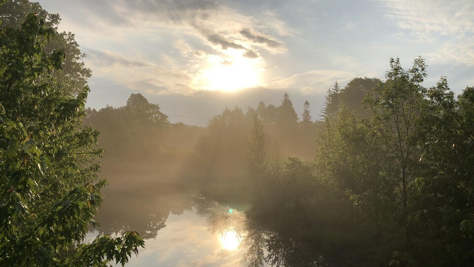 Le soleil est à l'orée des nuages et se reflète sur l'eau de la rivière.