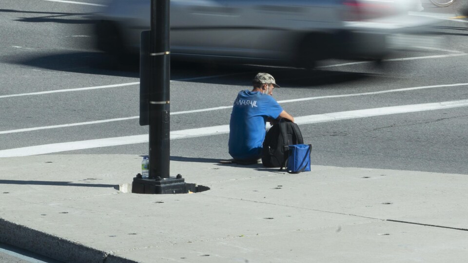 Un homme assis sur un terre-plein au milieu de la circulation.