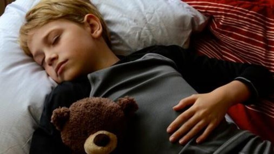Un garçon d'environ 12 ans qui dort avec un ourson en peluche.
