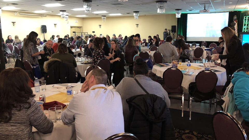 Des gens assis autour de plusieurs tables dans une salle de réception.