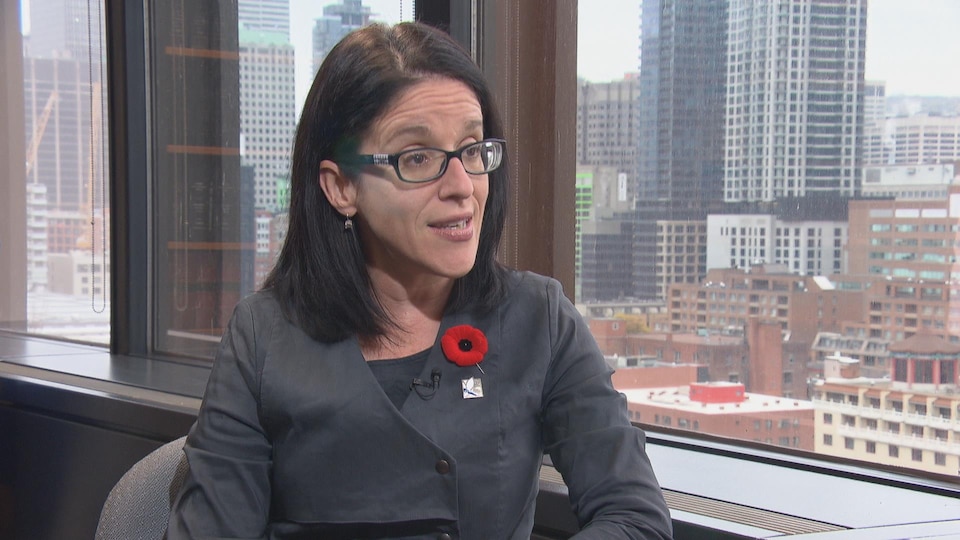 La ministre de la Justice Sonia Lebel est assise dans son bureau. On aperçoit, en arrière-plan, le centre-ville de Montréal.